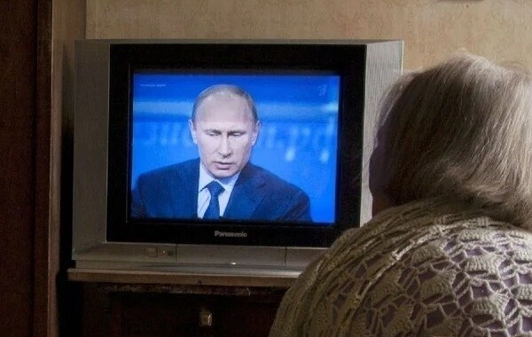 Старшая женщина наблюдает, как Путин выступает в телевизоре.